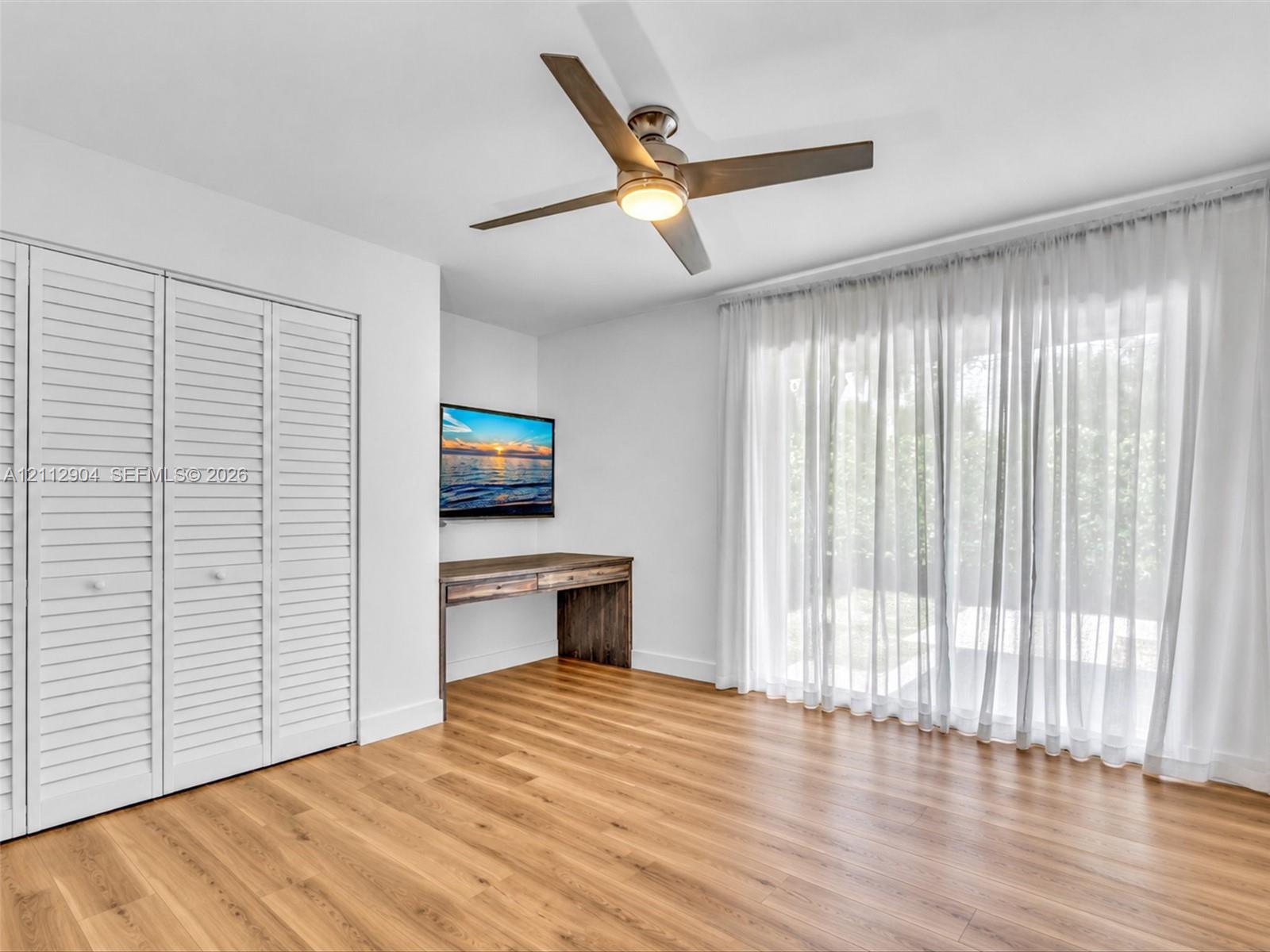 Wood-finish flooring, white louvered-style closet doors, modern ceiling fan with integrated lighting, and floor-to-ceiling glass sliding doors