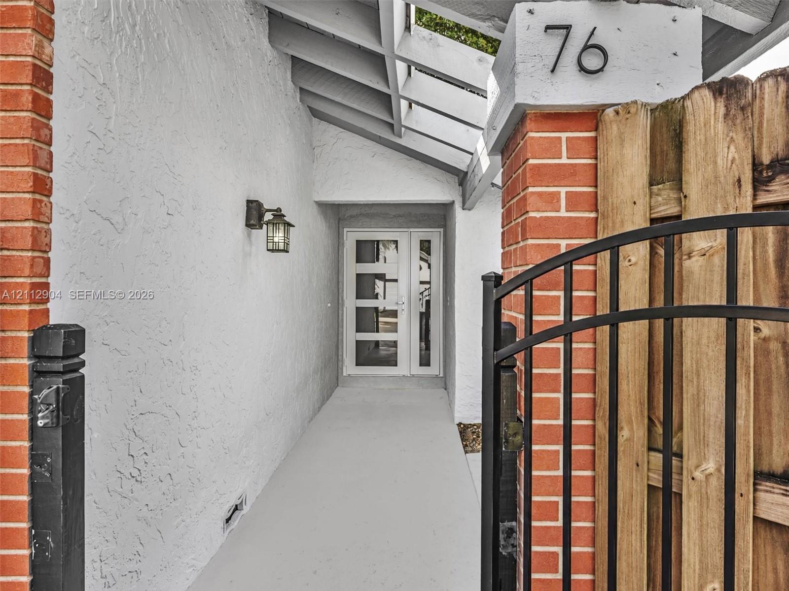 Covered entryway featuring a brick-accented stucco facade, open-beam ceiling, metal gate, and a multi-panel glass-inset entry door