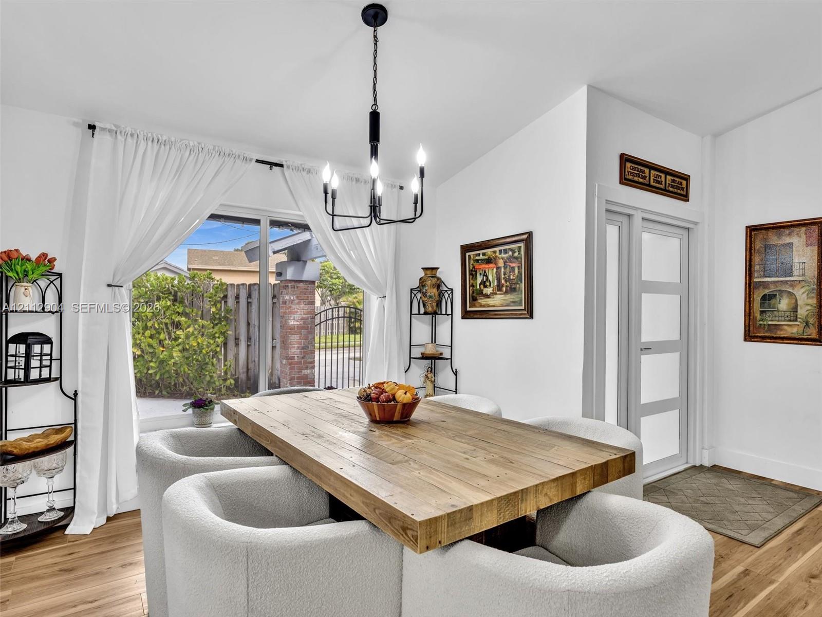 Dining area featuring wood-finish flooring, a five-light matte black chandelier, and a multi-panel glass door with frosted inserts