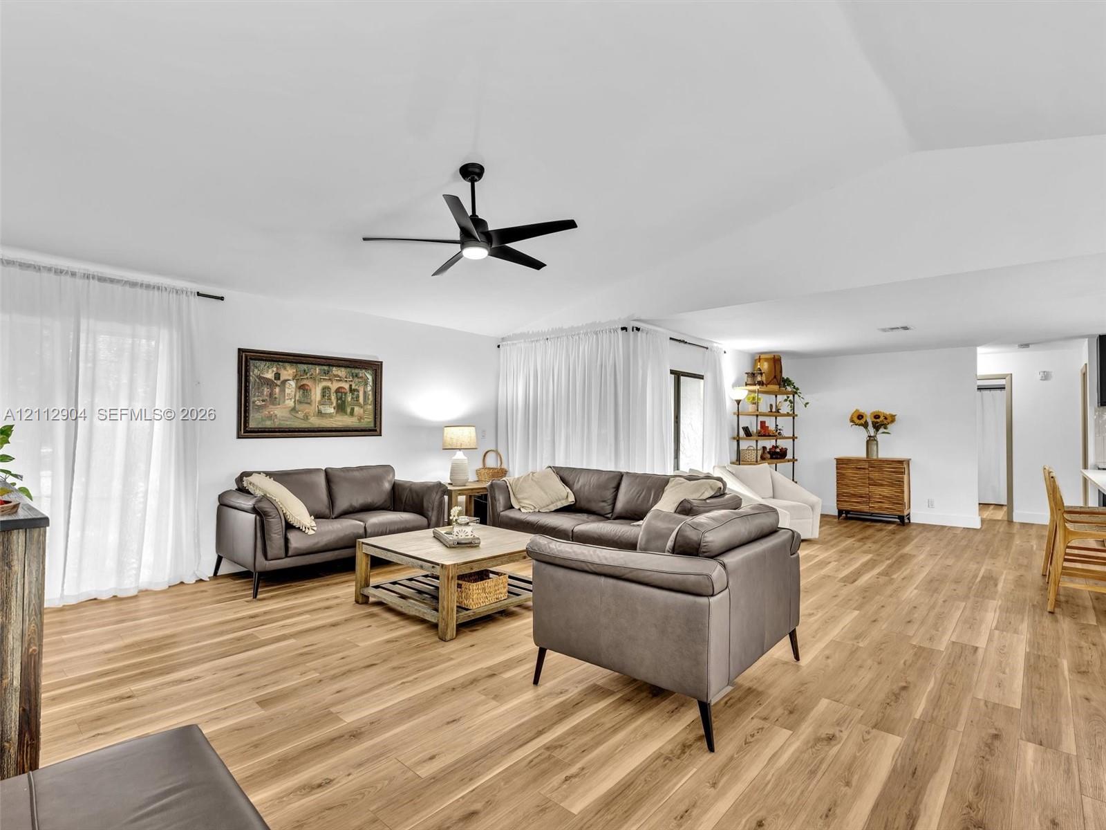 Living area featuring wood-finish flooring, vaulted ceilings, and a central matte black ceiling fan