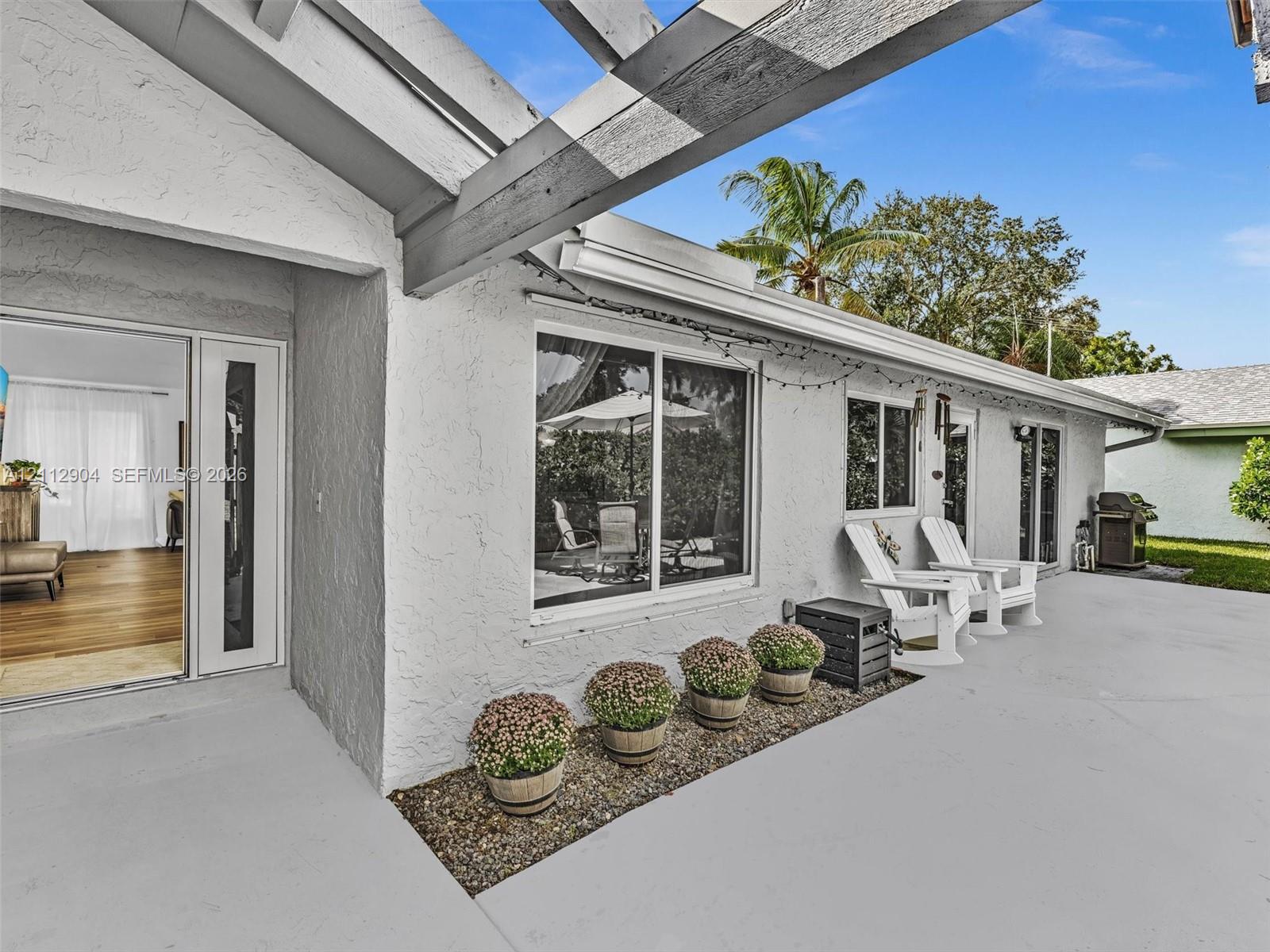 Stucco exterior patio featuring a wood-beam pergola, concrete flooring, and a stone-lined garden bed