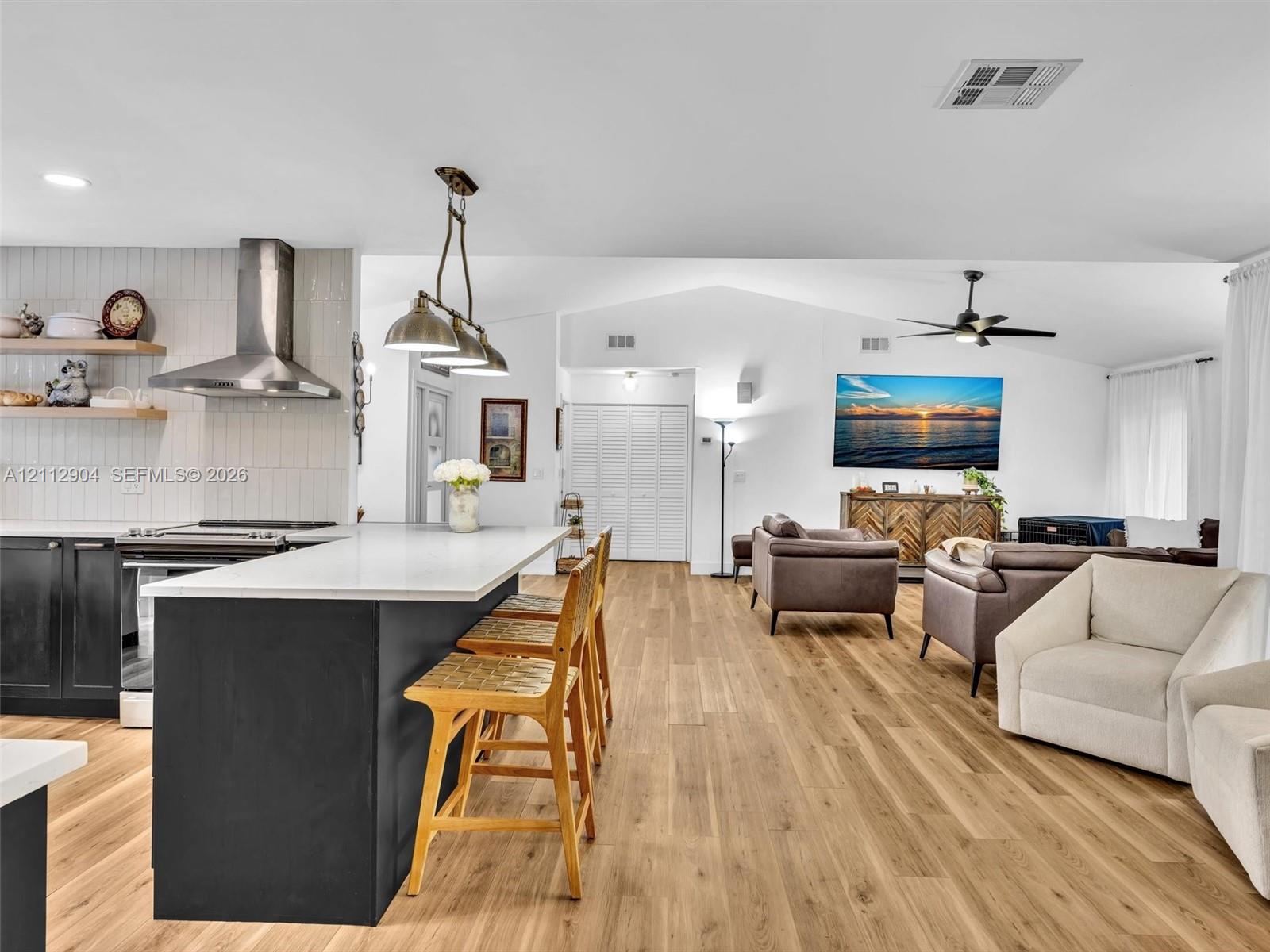 Kitchen featuring a central island with a quartz countertop, stainless steel range hood, vertical tiled backsplash, wood-finish flooring, and industrial-style pendant lighting