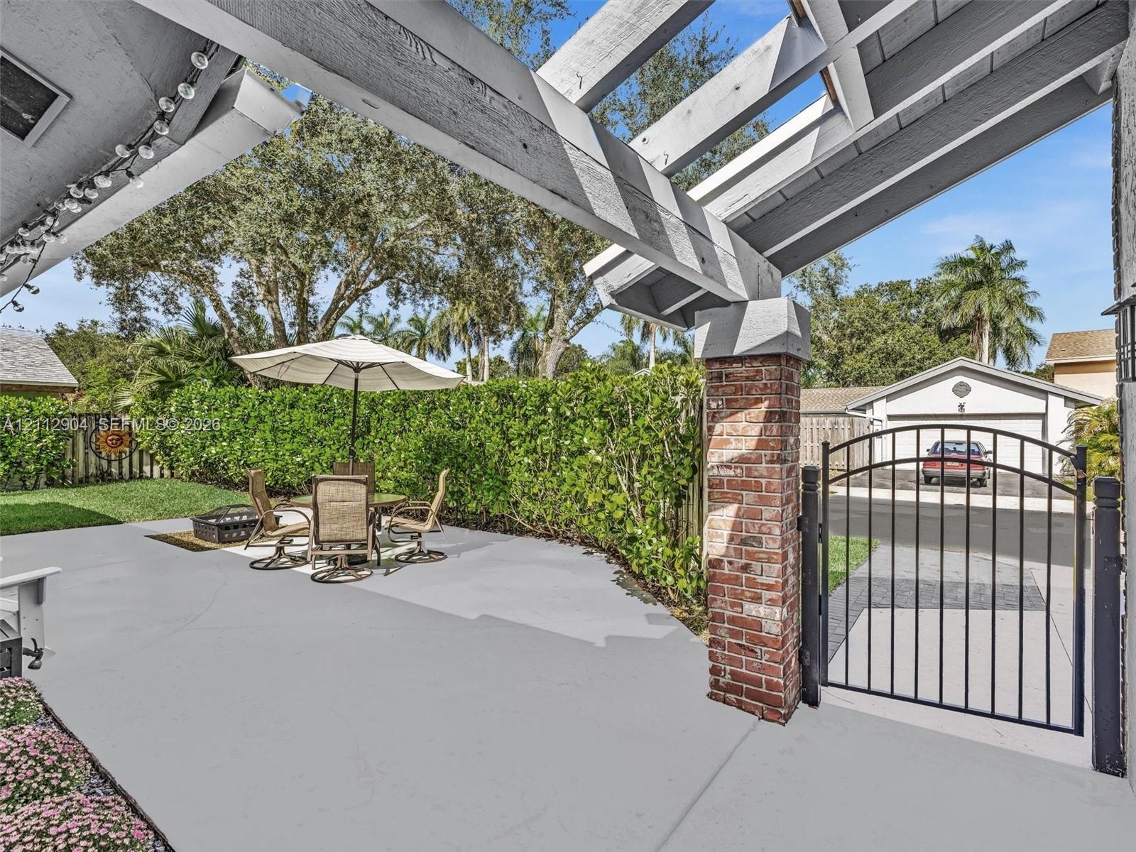 Covered patio featuring a timber-frame pergola, brick-pillar architectural detailing, and a black metal pedestrian gate