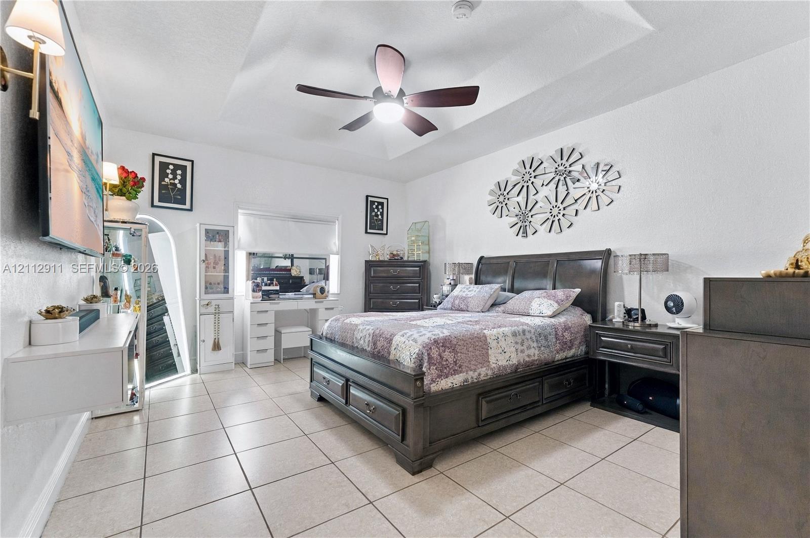 Tray ceiling featuring a central lighted ceiling fan, complemented by tile flooring, an arched mirror installation, and wall-mounted lighting fixtures