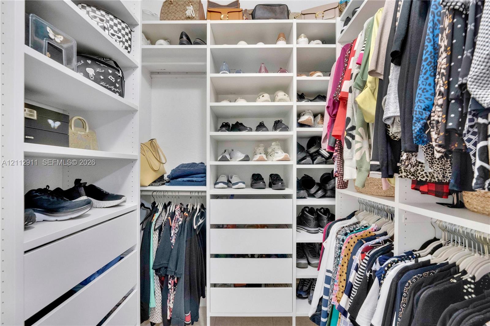 Custom walk-in closet featuring white built-in cabinetry, multiple adjustable shelving tiers, integrated drawer storage, and dual-level hanging rods