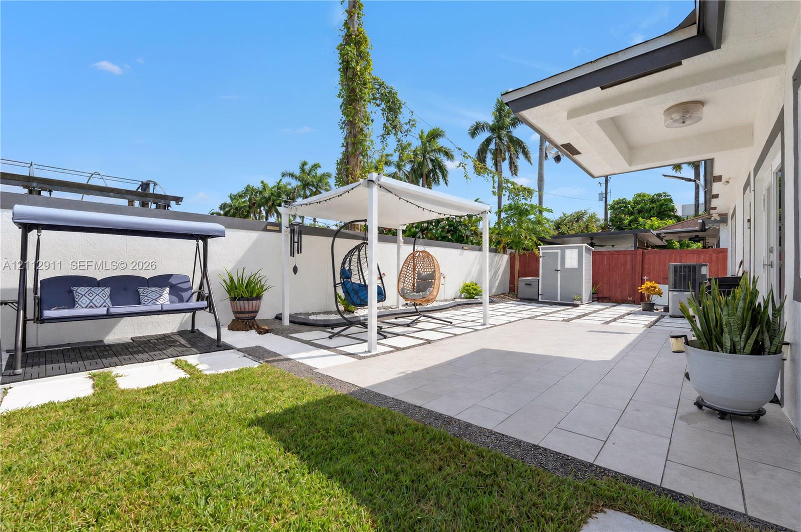 Backyard featuring a paved patio with geometric stone inlay, a covered pergola structure, a solid perimeter wall, and a maintained lawn area