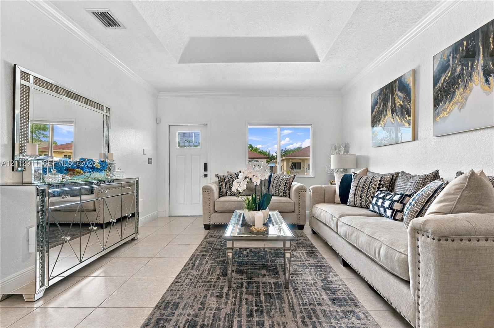 Living area featuring a tray ceiling, crown molding, neutral tile flooring, and a single-light entry door