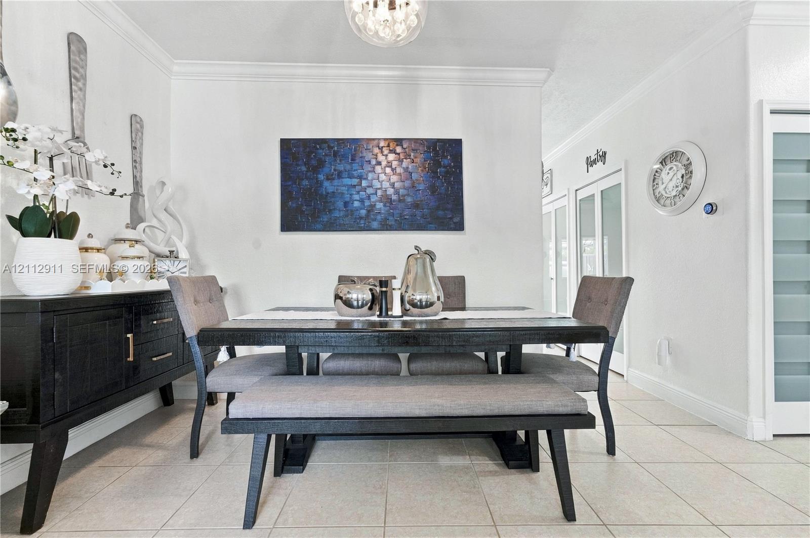 Dining area featuring neutral tile flooring, crown molding, and a spherical glass-shade pendant light