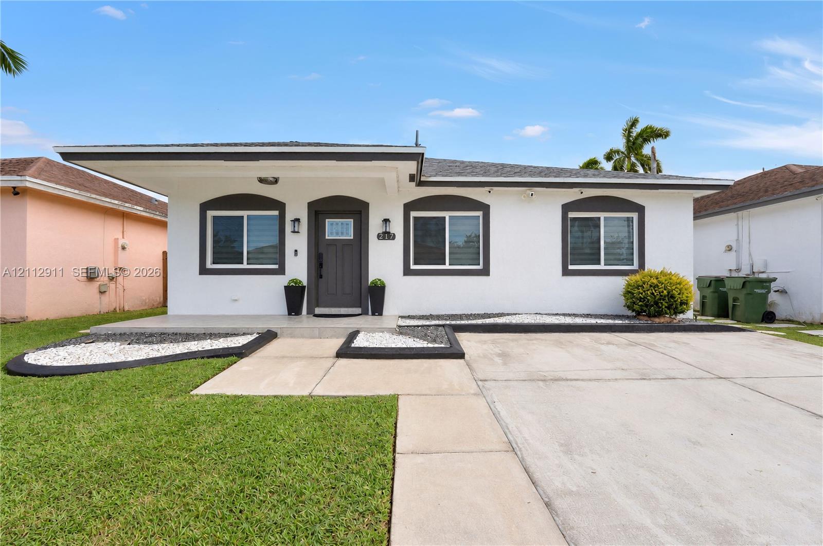 Single-story exterior featuring a covered front porch, arched window trim, concrete driveway, and minimalist landscape design with stone-accented beds