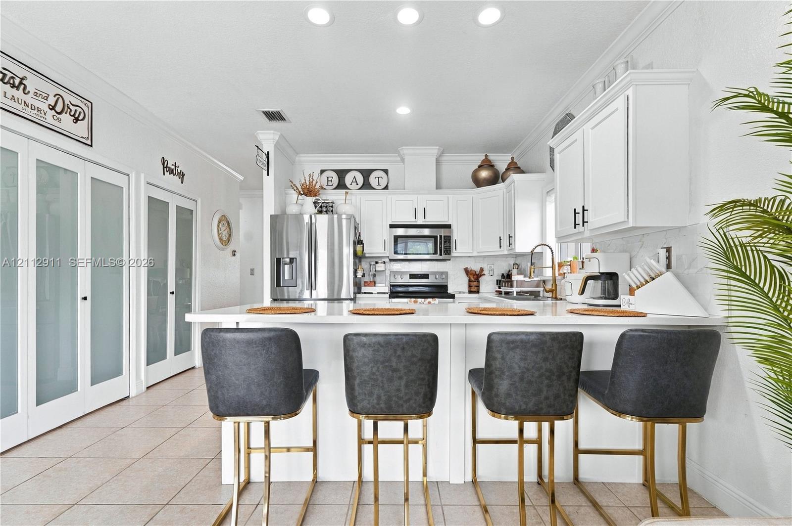 Kitchen featuring white cabinetry, solid-surface countertops, stainless steel appliances, recessed lighting, and dual frosted-glass pantry doors