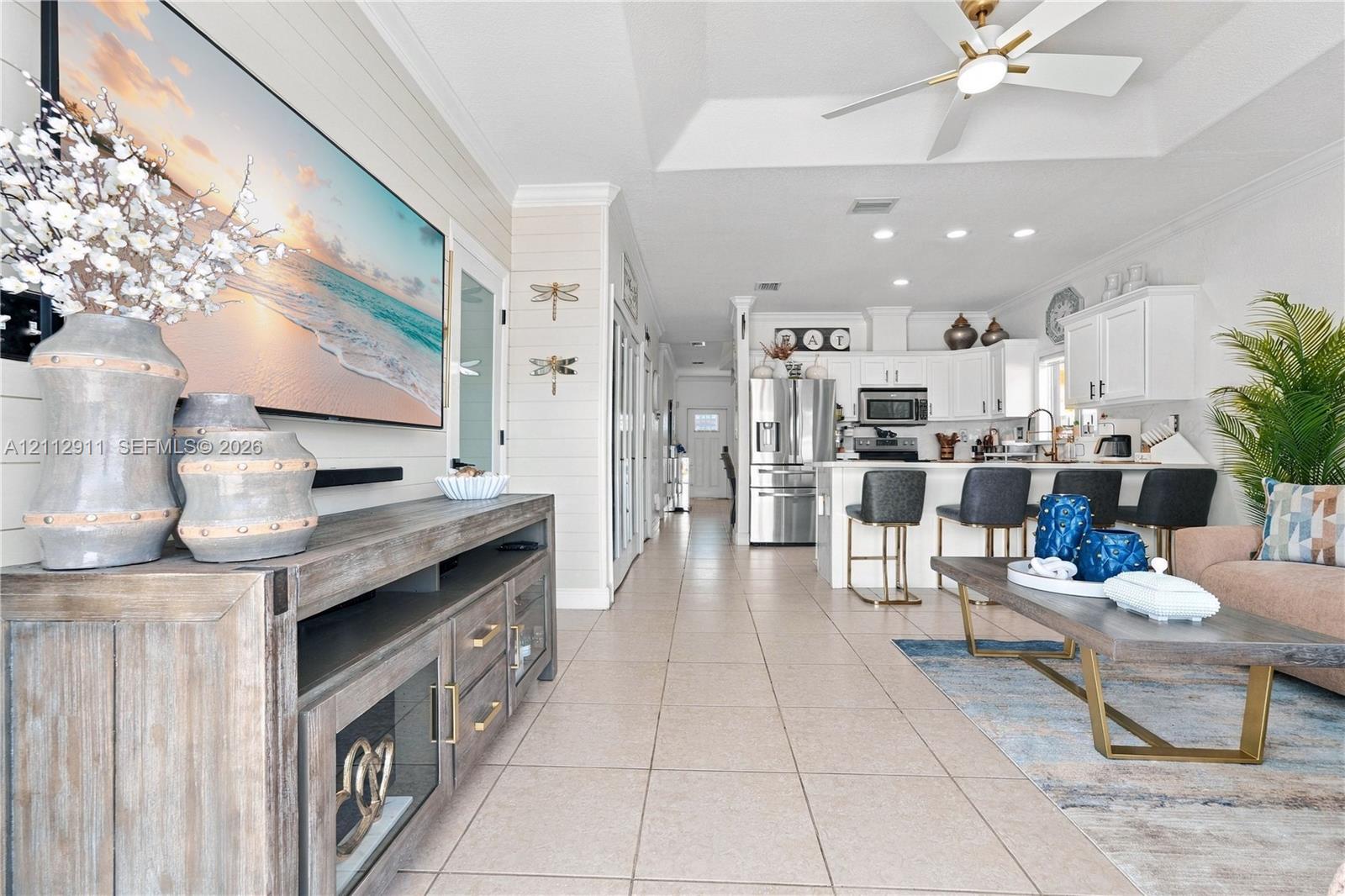 Open-concept floor plan featuring a trey ceiling, tile flooring, shiplap wall accents, recessed lighting, and a kitchen island with built-in cabinetry