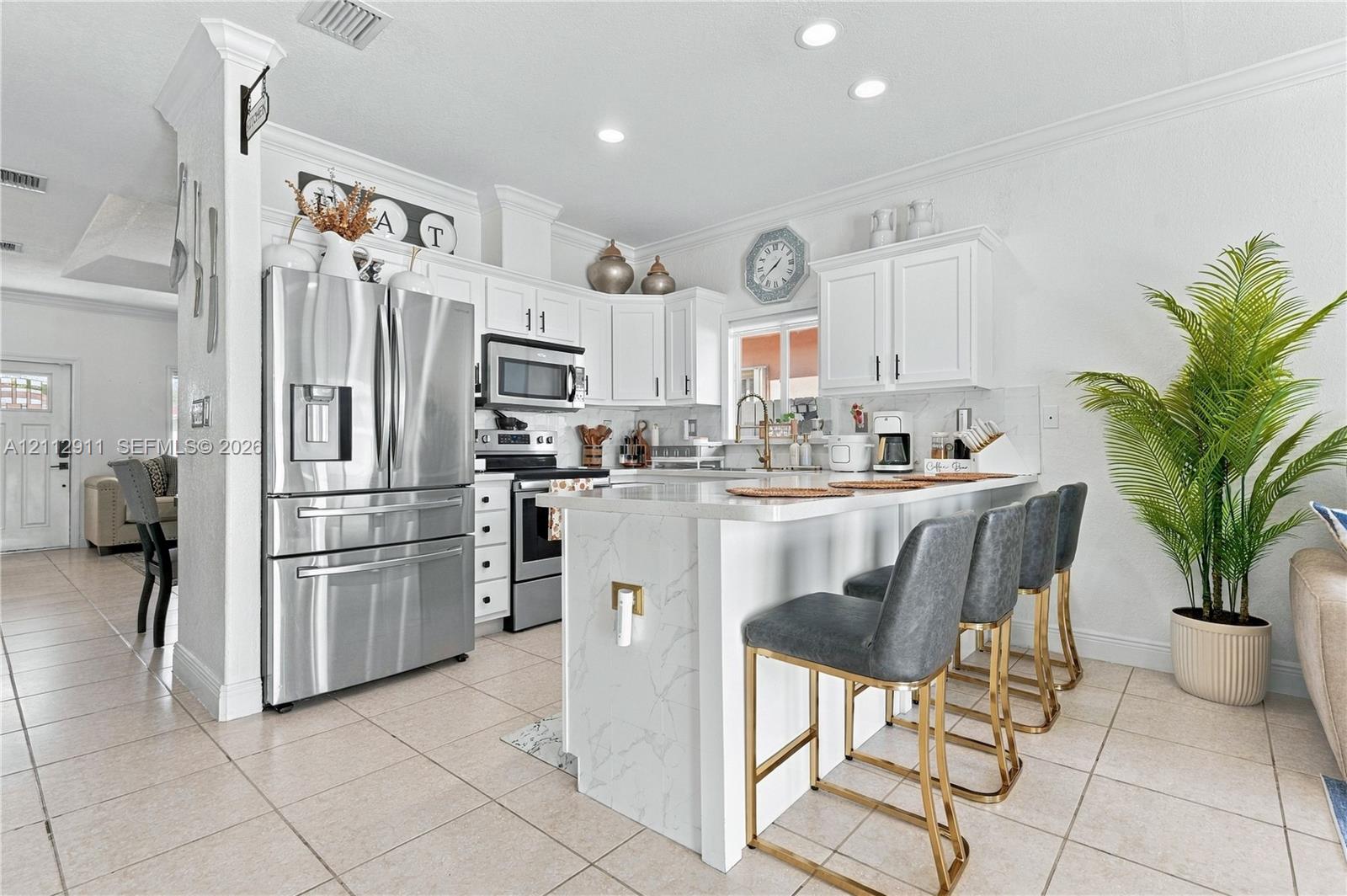 Kitchen featuring white cabinetry, stone-finish waterfall edge island, tile flooring, recessed lighting, and stainless steel appliances