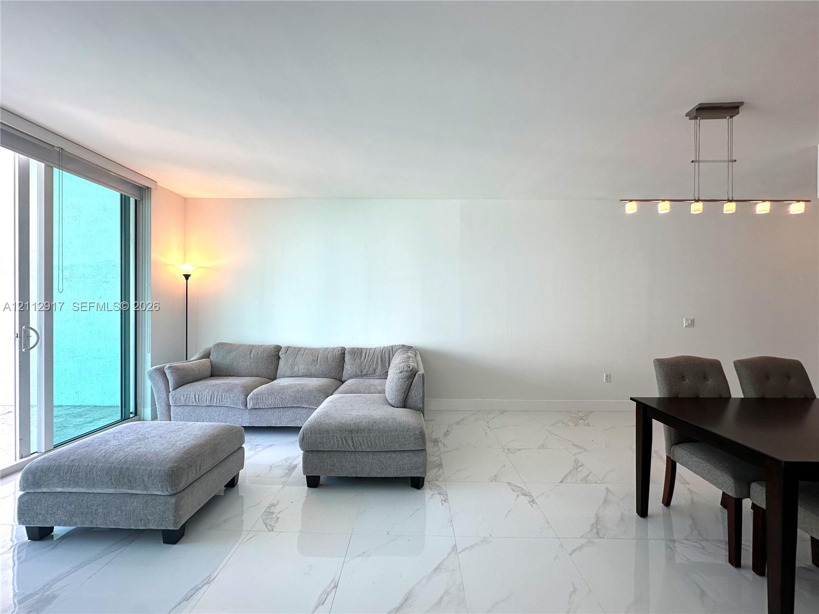 Large-format polished tile flooring featuring a vein-patterned finish, full-height sliding glass doors, and a linear multi-light pendant fixture with a brushed metal finish