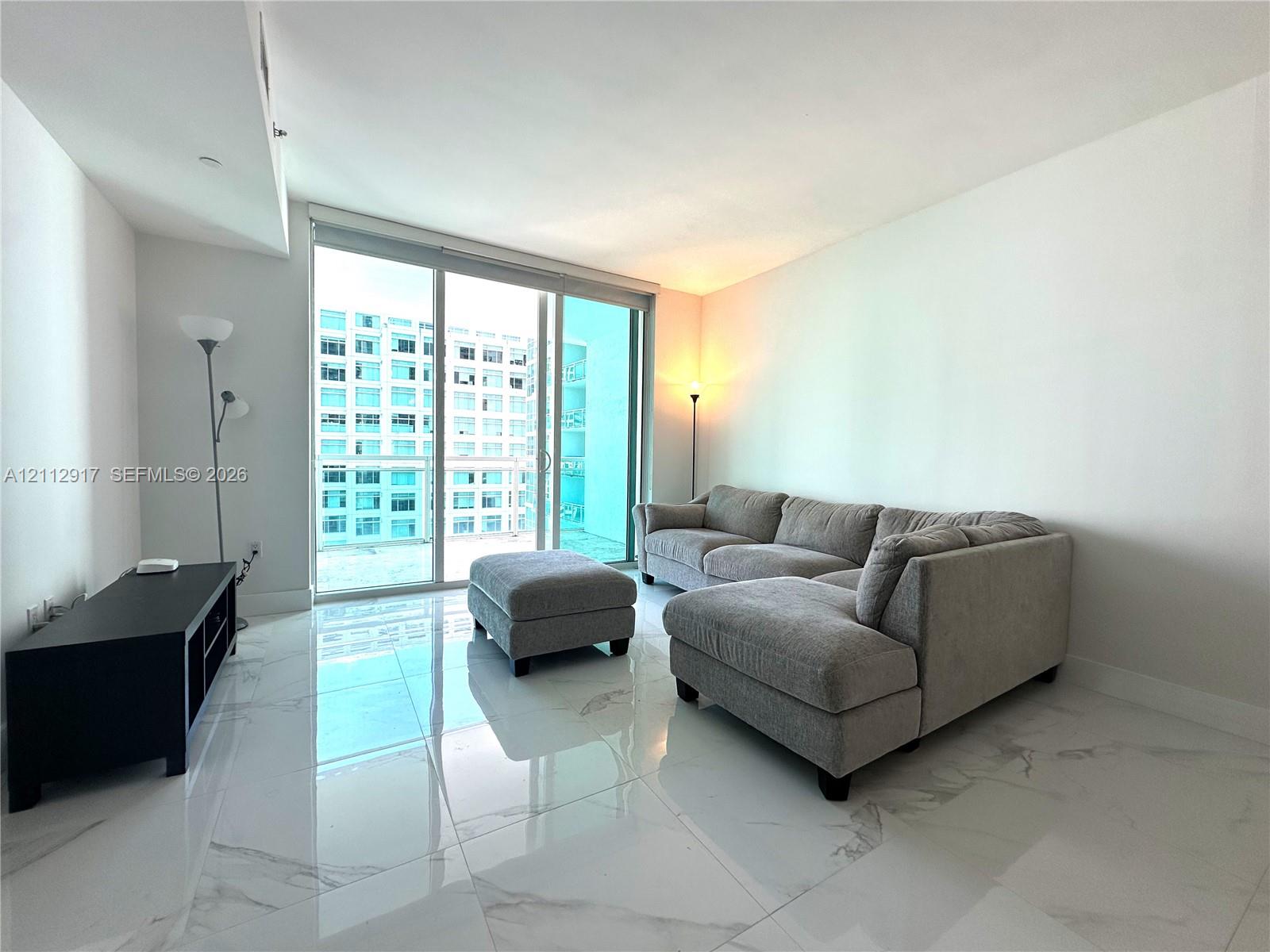 Large-format polished stone flooring with white and grey veining, floor-to-ceiling glass sliding doors, and private balcony access