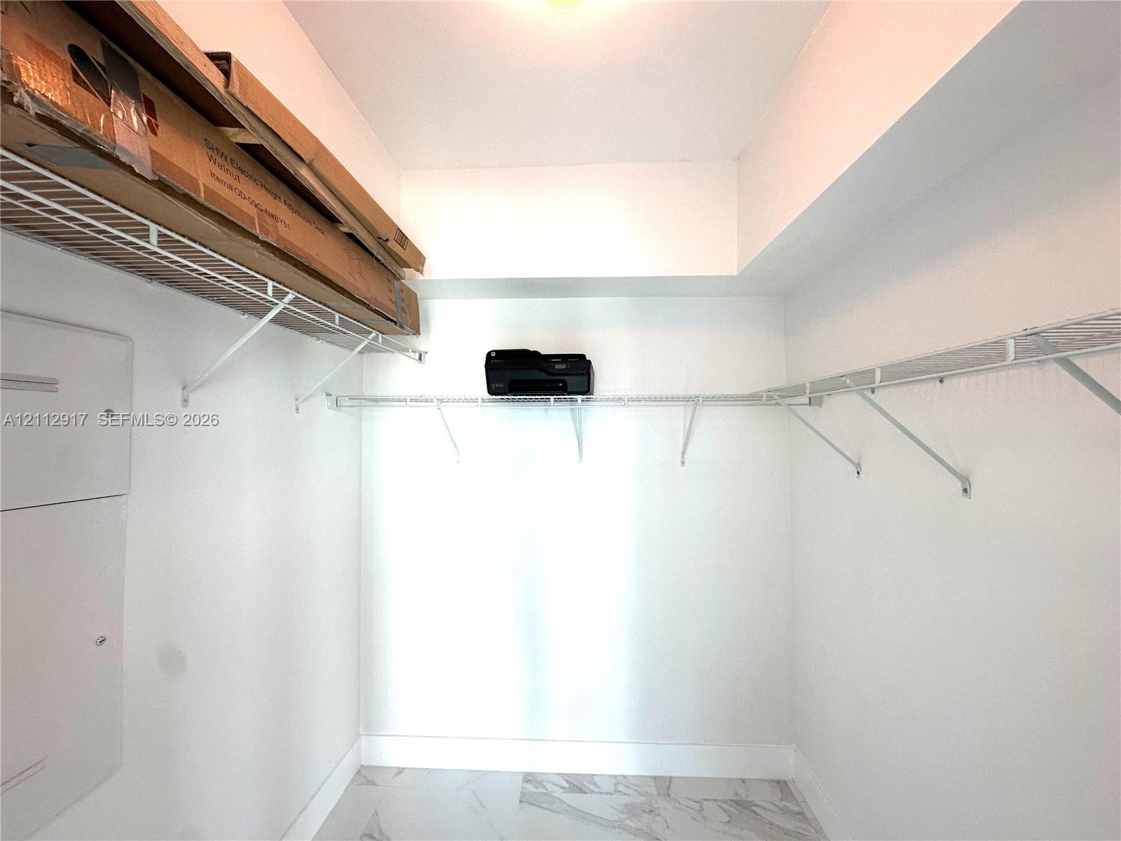 Walk-in closet featuring white walls, stone-finish flooring, and tiered wire shelving