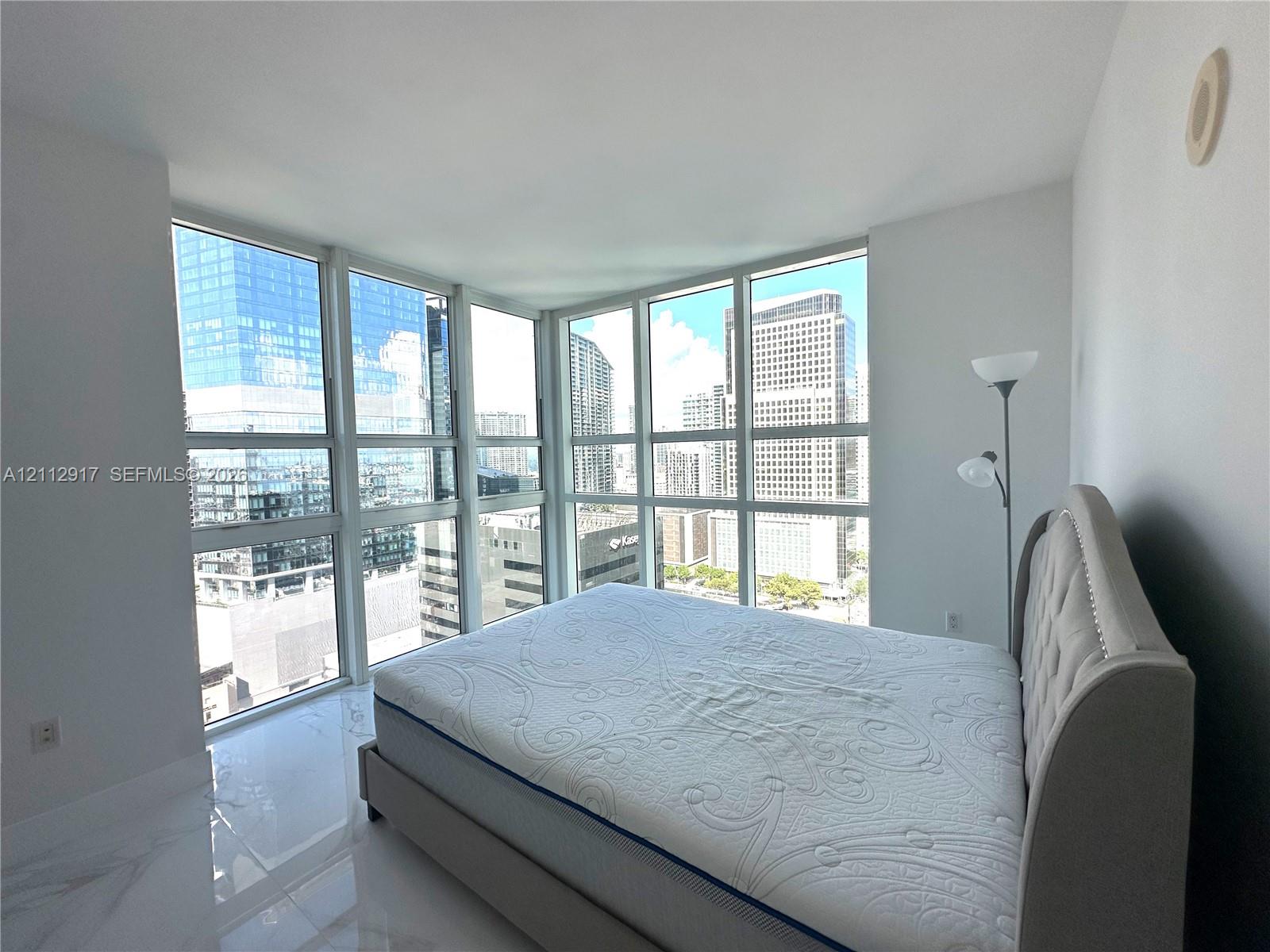 Interior featuring polished stone-finish flooring, white walls, and floor-to-ceiling multi-pane windows showcasing urban architecture
