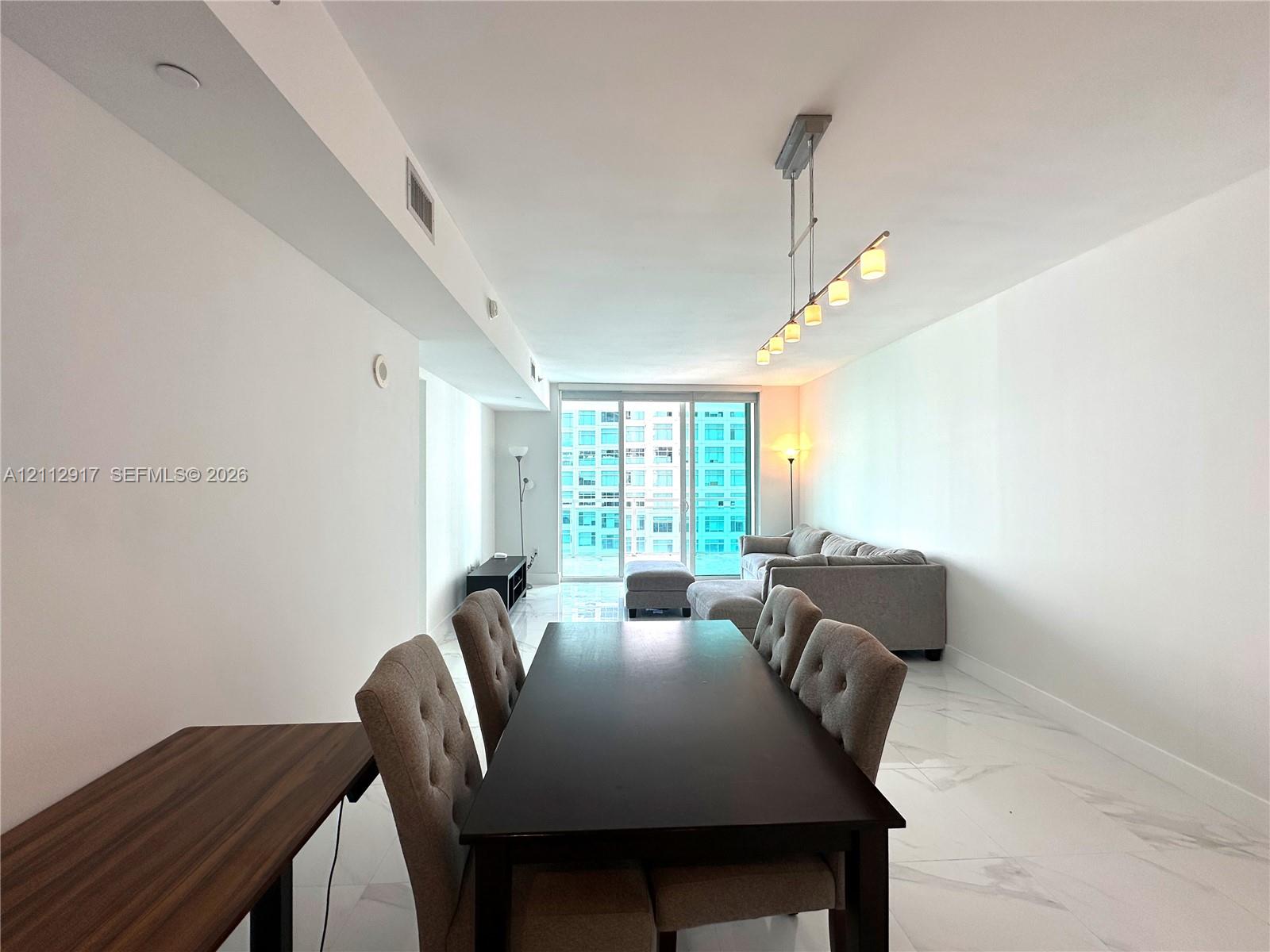 Polished stone flooring, linear multi-light pendant fixture, and floor-to-ceiling glass sliding doors