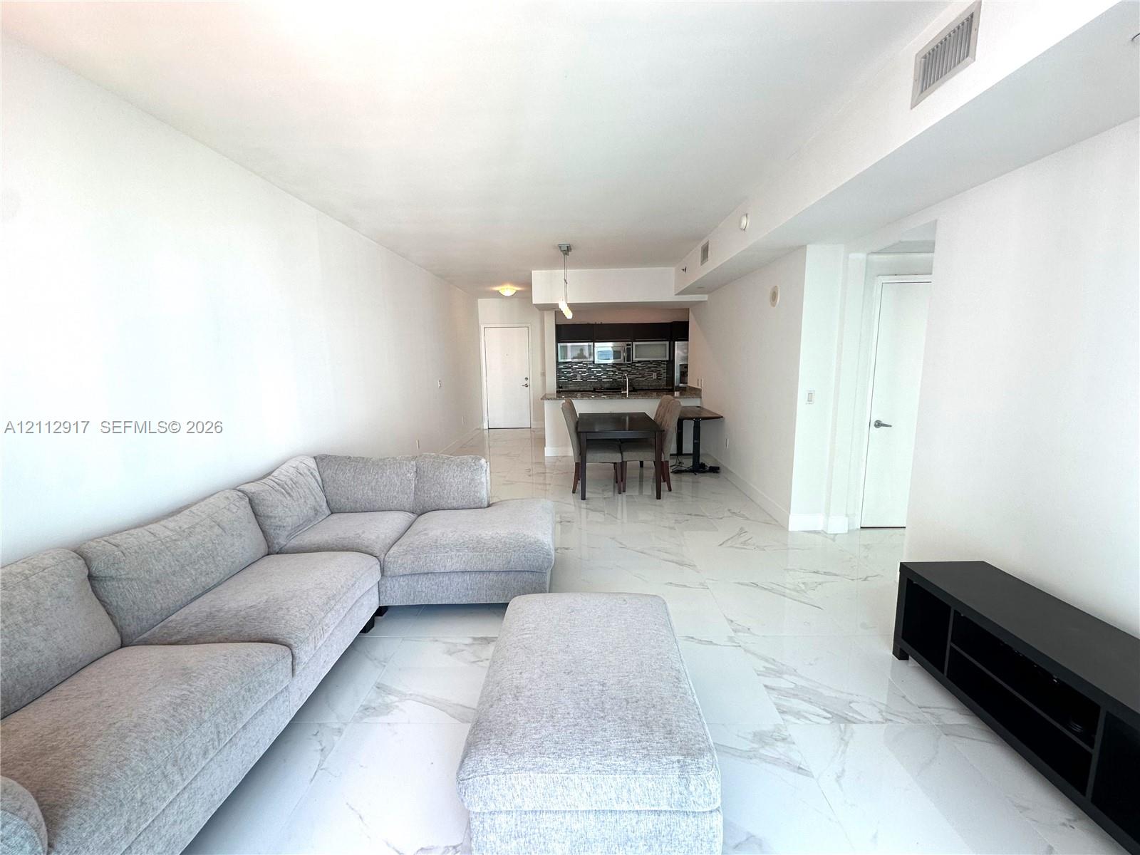 Open-concept floor plan featuring large-format polished flooring with veined detailing and a built-in kitchen peninsula