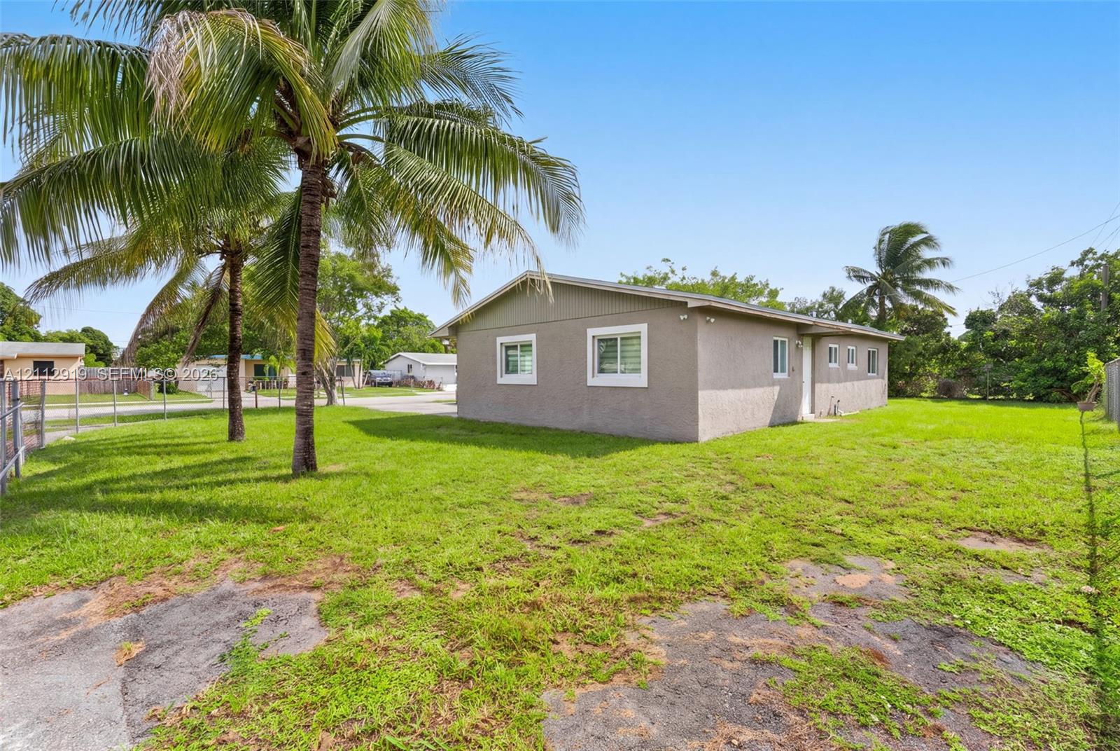 Stucco exterior siding, single-story profile, multi-pane windows, and mature palm trees set on a grass lot