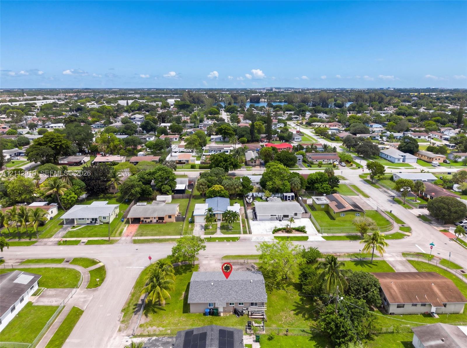 Aerial perspective of a corner lot residence featuring a pitched shingle roof, expansive grass lawn, and mature palm trees