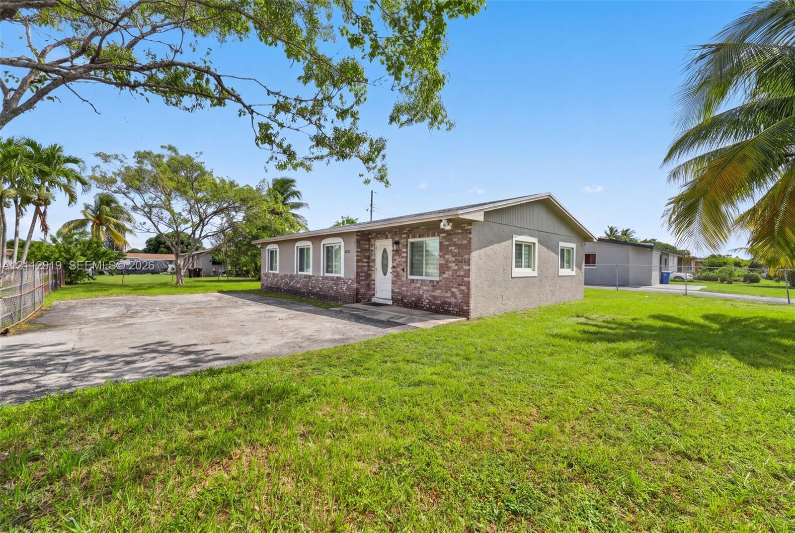 Single-story exterior featuring a partial brick facade, stucco finish, paved driveway, and multiple casement windows