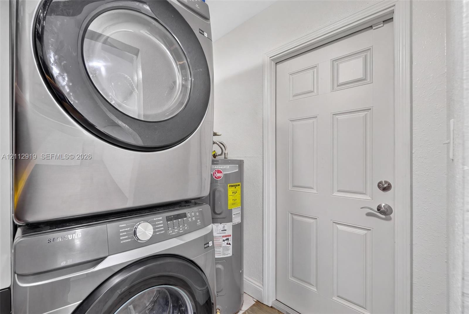 Stacked stainless steel front-load laundry appliances and a vertical water heater paired with a six-panel interior door featuring satin nickel hardware