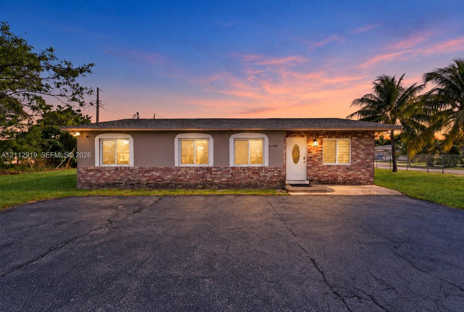 Single-story exterior featuring a brick facade base, stucco upper walls, arched window trim, and a paved asphalt driveway Single-story exterior featuring a brick facade base, stucco upper walls, arched window trim, and a paved asphalt driveway