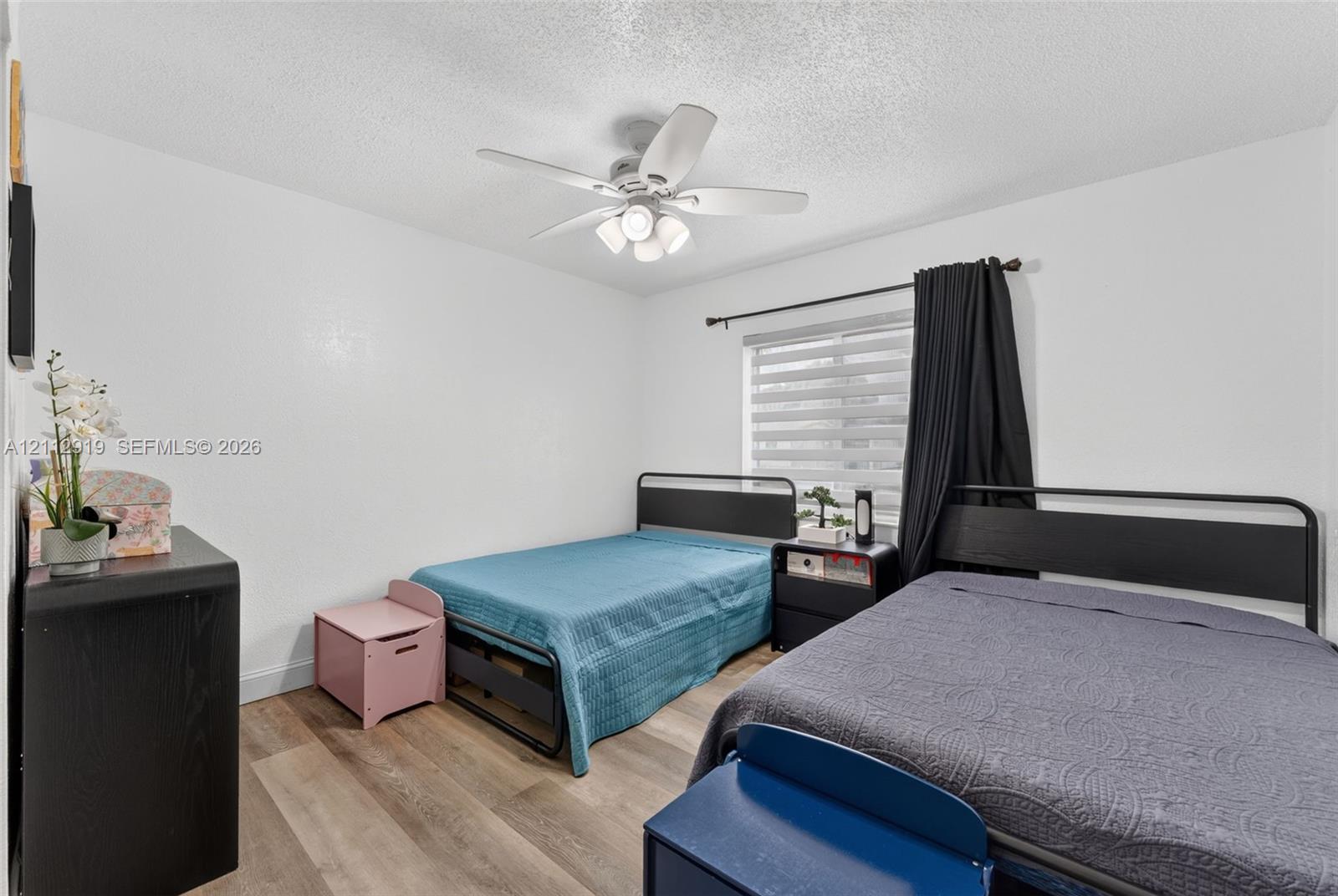 Interior room featuring wood-finish flooring, a ceiling fan with integrated lighting, textured ceiling, a window with horizontal blinds, and a built-in electrical outlet