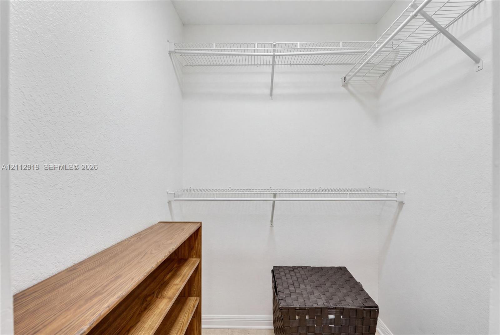 Walk-in storage space featuring dual-tier coated wire shelving and a built-in wood-finish shelving unit