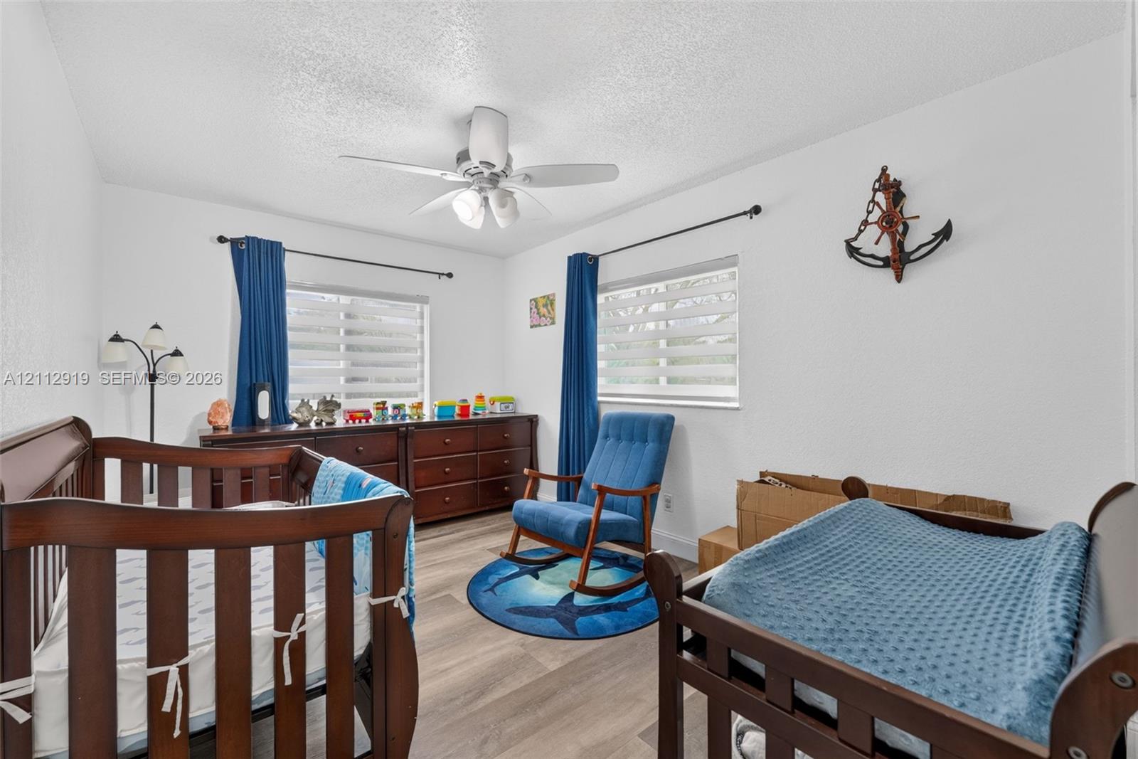 Wood-finish flooring, dual windows with fitted shades, and a ceiling-mounted light fixture with a fan