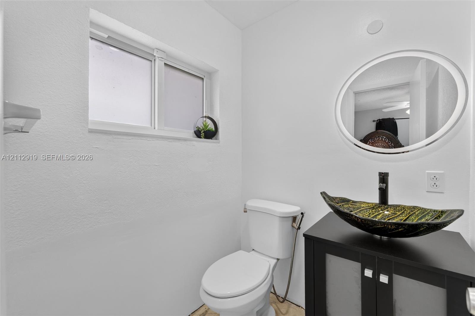 Bathroom featuring a dark wood-finish vanity, decorative vessel sink, black faucet, oval wall mirror, and sliding window