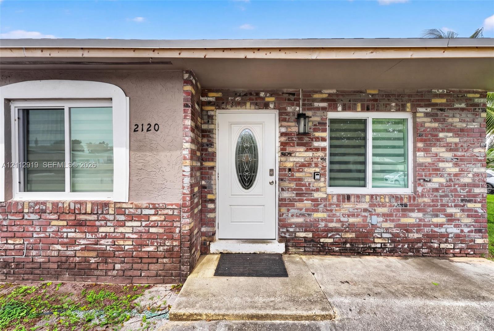 Exterior facade featuring multi-tone brick masonry, smooth-finish stucco, a white entry door with an oval glass insert, and sliding windows