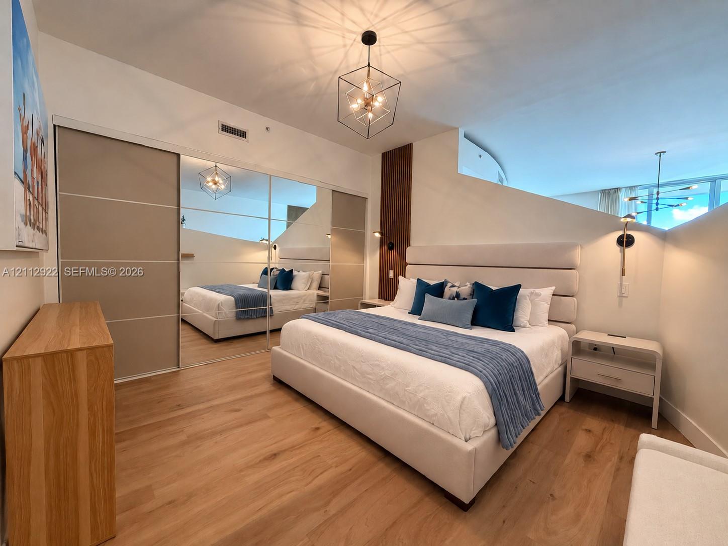 Wood-finish flooring, floor-to-ceiling mirrored closet doors, geometric pendant lighting, and wall-mounted accent sconces
