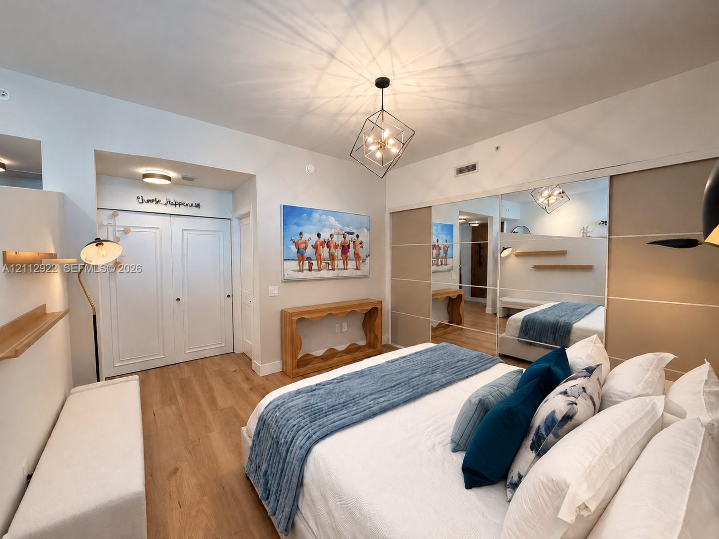 Interior featuring wood-finish flooring, geometric chandelier, built-in dual-panel closet, full-height mirrored closet doors, and floating wall shelves