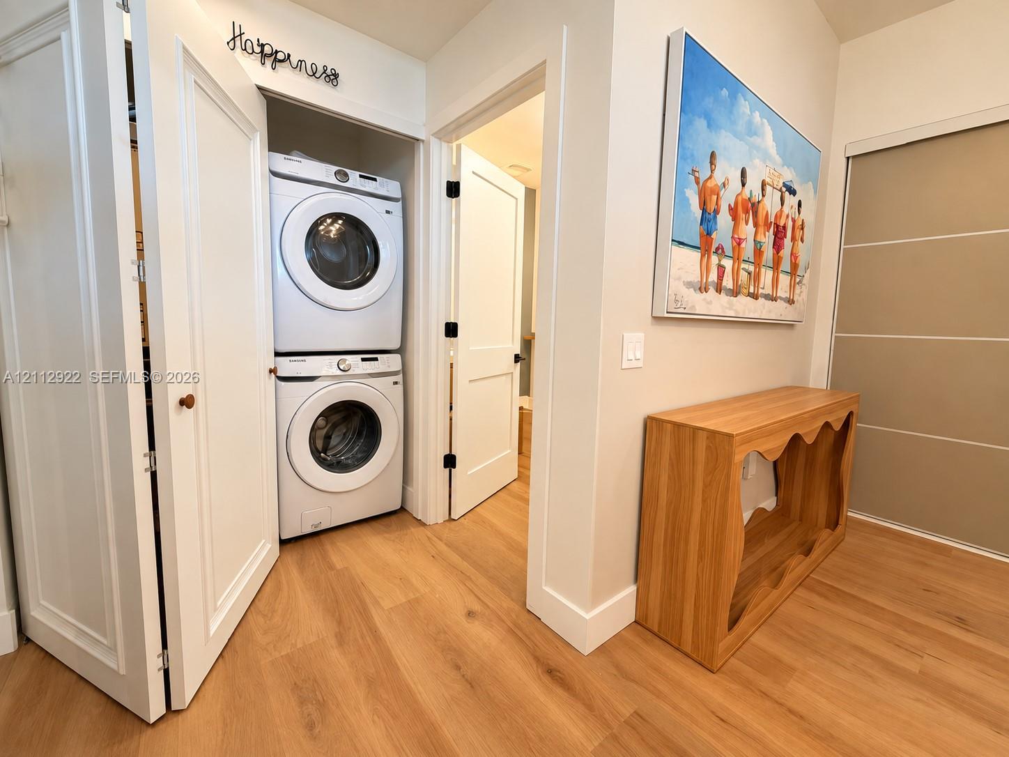 Laundry area featuring a stacked washer and dryer unit, wood-finish flooring, shaker-style interior doors, and a sliding-panel door closet