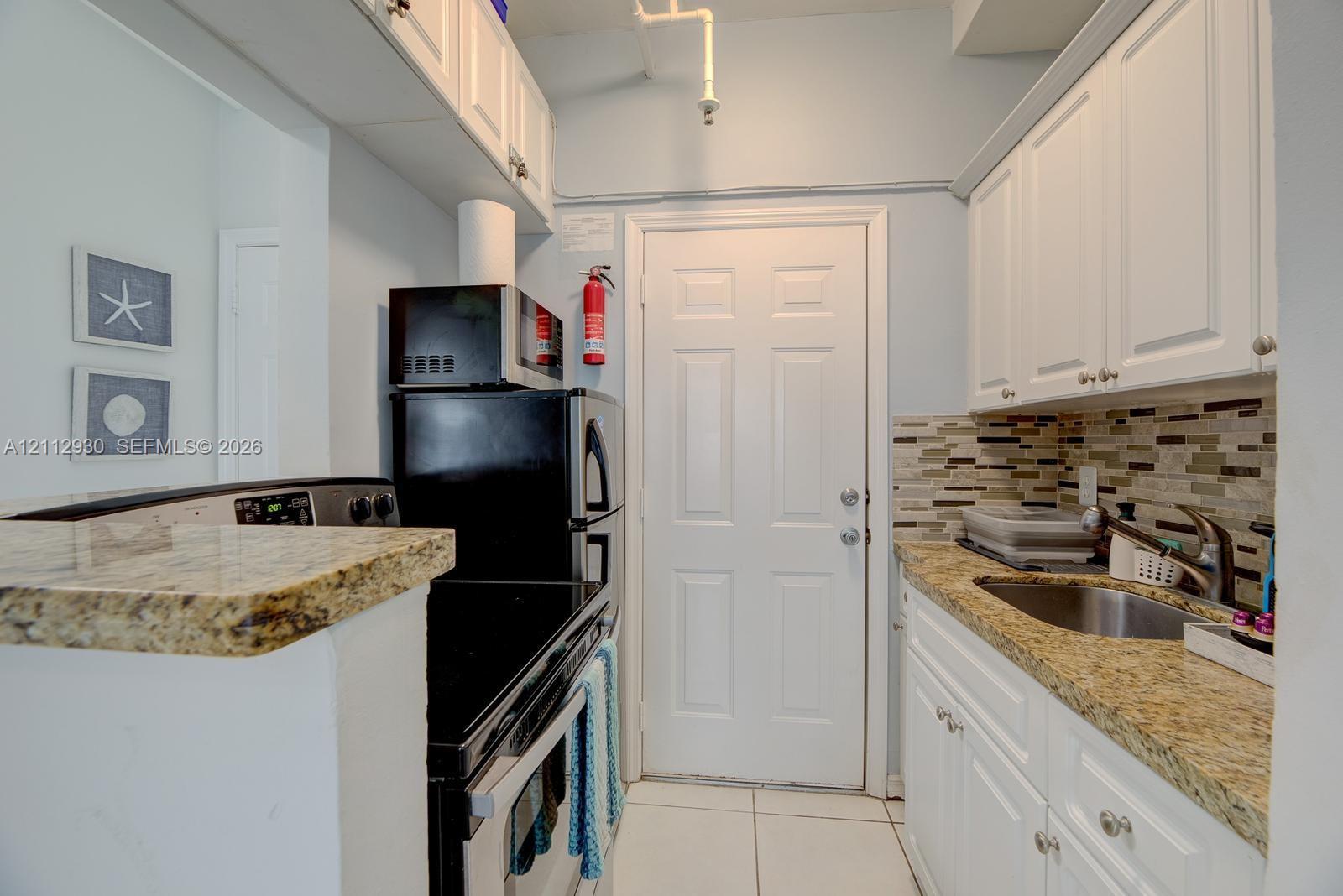 Kitchen featuring white cabinetry, stone-finish countertops, tile backsplash, stainless steel sink, and tile flooring