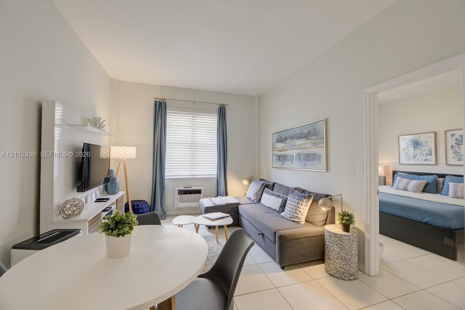 Interior living space featuring large-format tile flooring, bright neutral wall tones, and a wall-mounted media console