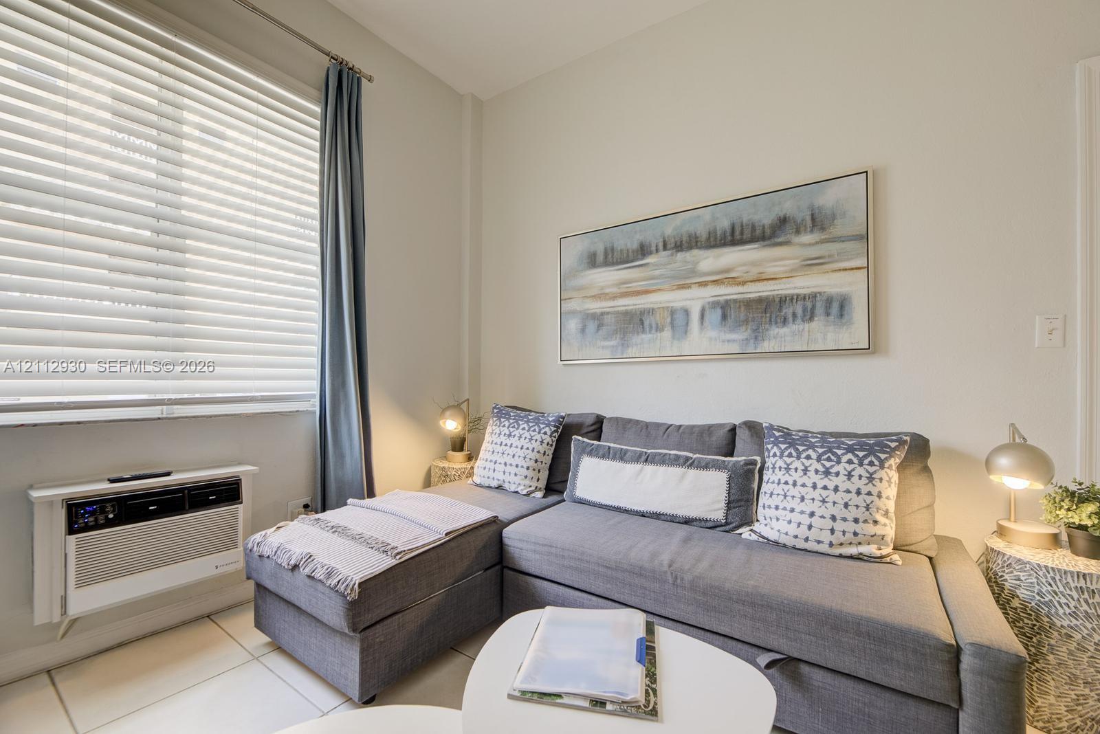 Neutral-toned interior featuring horizontal window blinds and a wall-mounted climate control unit