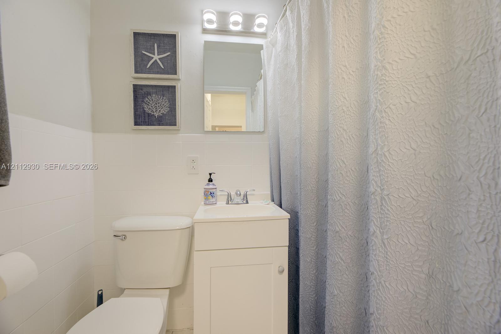 Bathroom featuring white cabinetry, a single-basin sink with a metallic faucet, a wall-mounted rectangular mirror, and a three-bulb light fixture