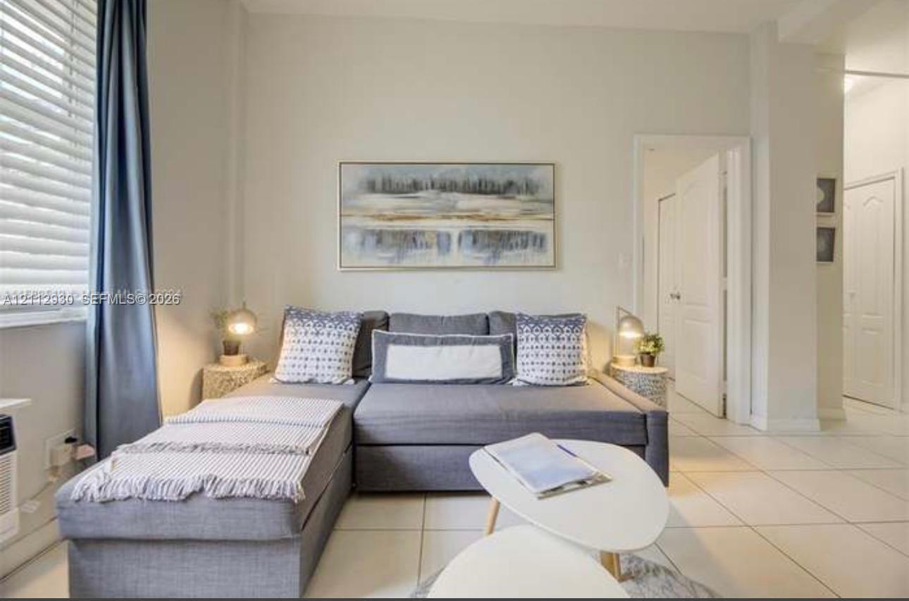 Living area featuring neutral-toned walls, large-format tile flooring, and multi-panel window blinds