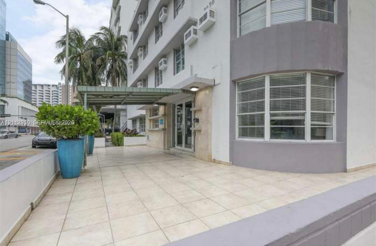 Exterior entrance featuring a covered porte-cochre, light-toned ceramic tile flooring, a glass-paneled entry door, and bay-style windows