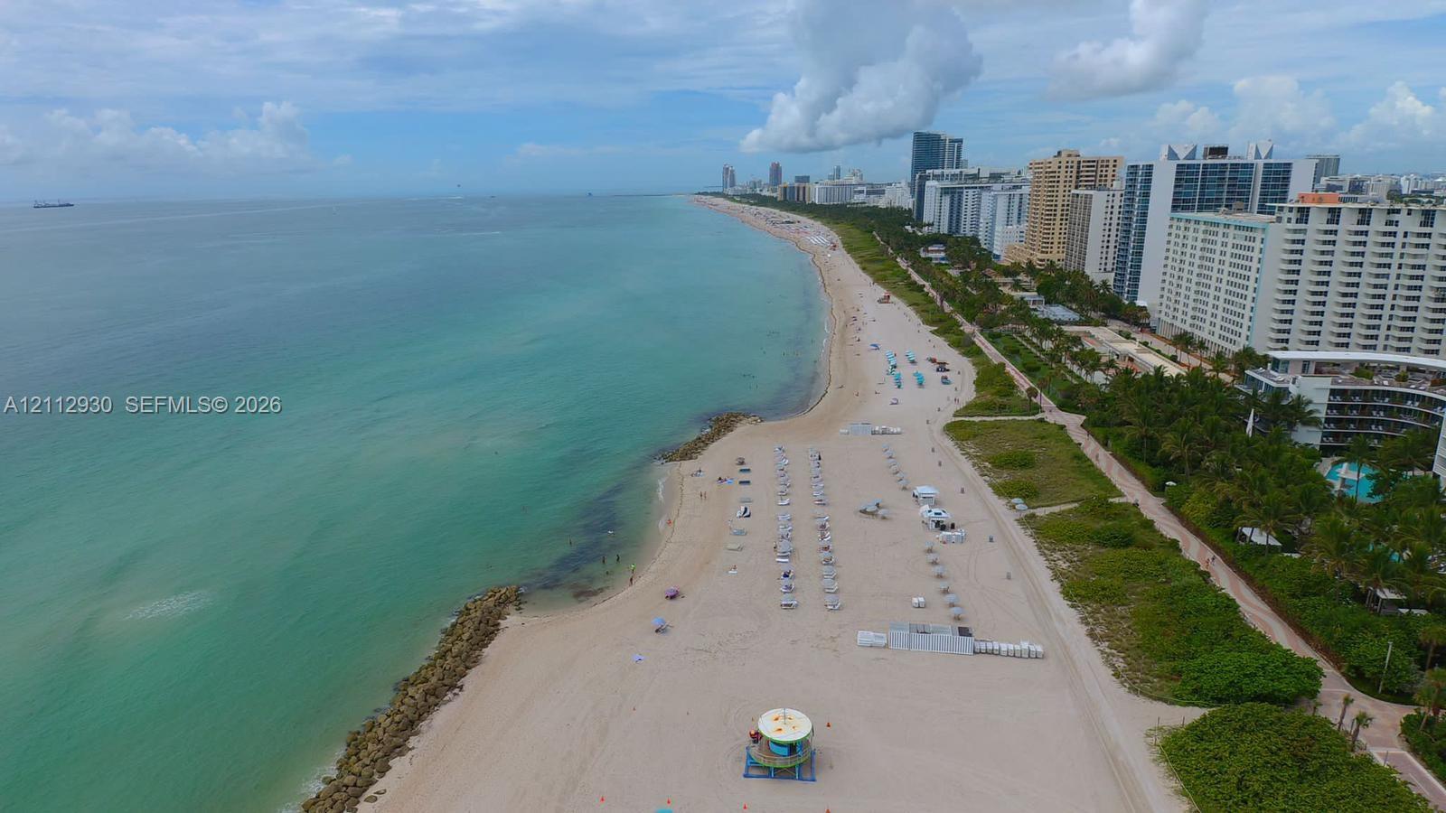 Aerial perspective featuring expansive sandy shoreline, turquoise coastal waters, and rock jetty elements
