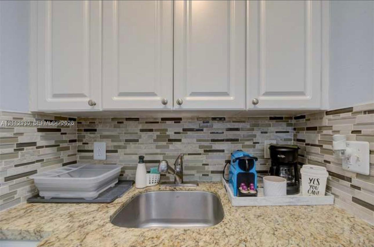 White cabinetry, stone-finish countertops, stainless steel undermount sink, gooseneck faucet, and multicolored linear glass tile backsplash