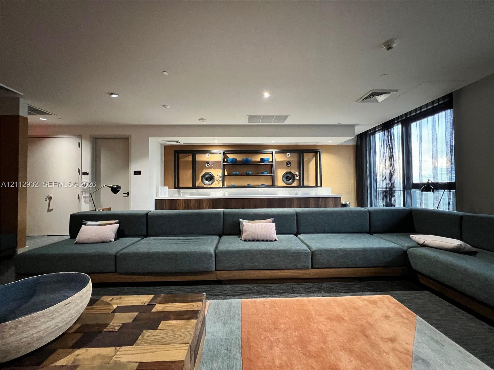 Built-in media console with wood-finish cabinetry, quartz countertop, and integrated shelving, featuring floor-to-ceiling windows with expansive glass panels and recessed ceiling lighting
