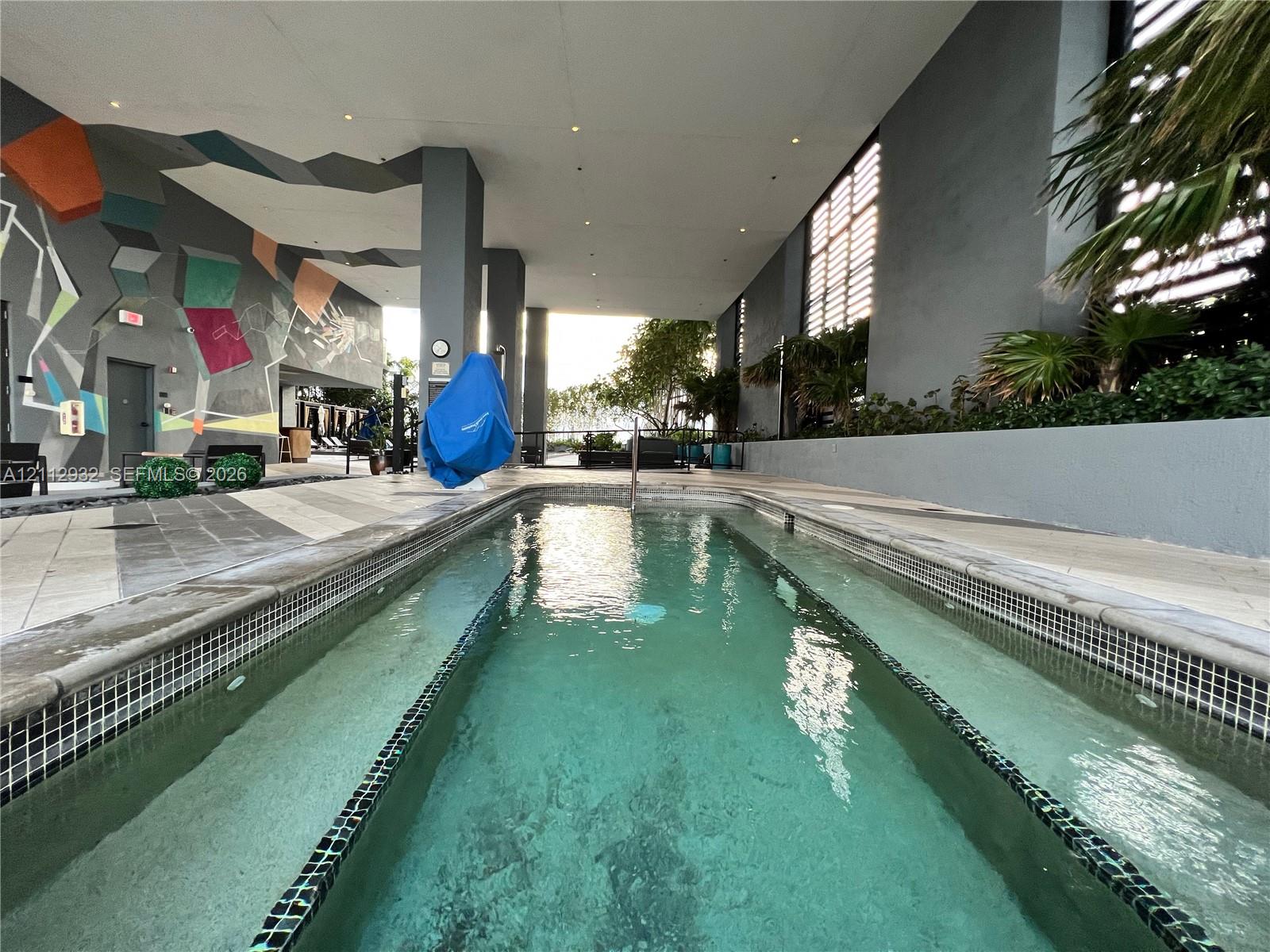 Covered swimming pool featuring tiled coping, geometric mural wall, recessed ceiling lighting, and large-format tile decking