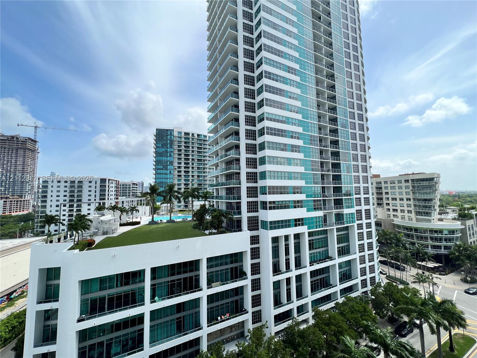High-rise glass and concrete tower featuring tiered balcony levels, a landscaped elevated terrace, and ground-level palm tree accents