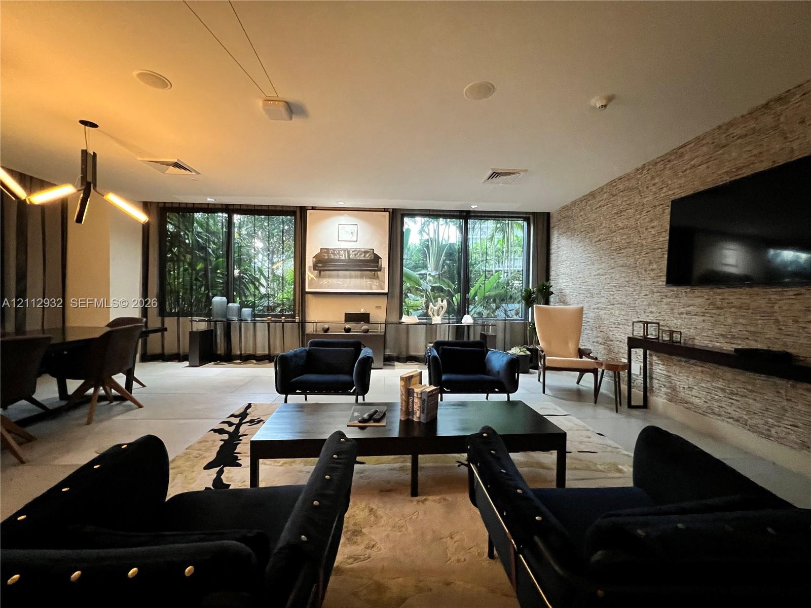 Living area featuring large-format tile flooring, textured stone accent wall, multi-panel sliding glass doors, contemporary geometric chandelier, and recessed ceiling lighting