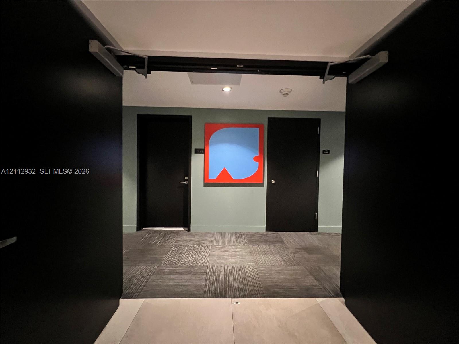 Hallway featuring high-contrast black paneled doors, square-patterned carpet, and a recessed ceiling light