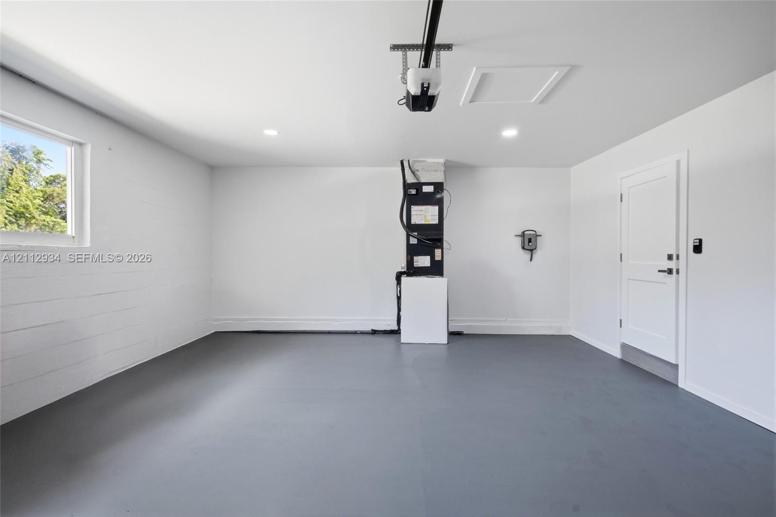 Finished garage featuring gray epoxy flooring, white painted walls, recessed lighting, and a solid-core interior door
