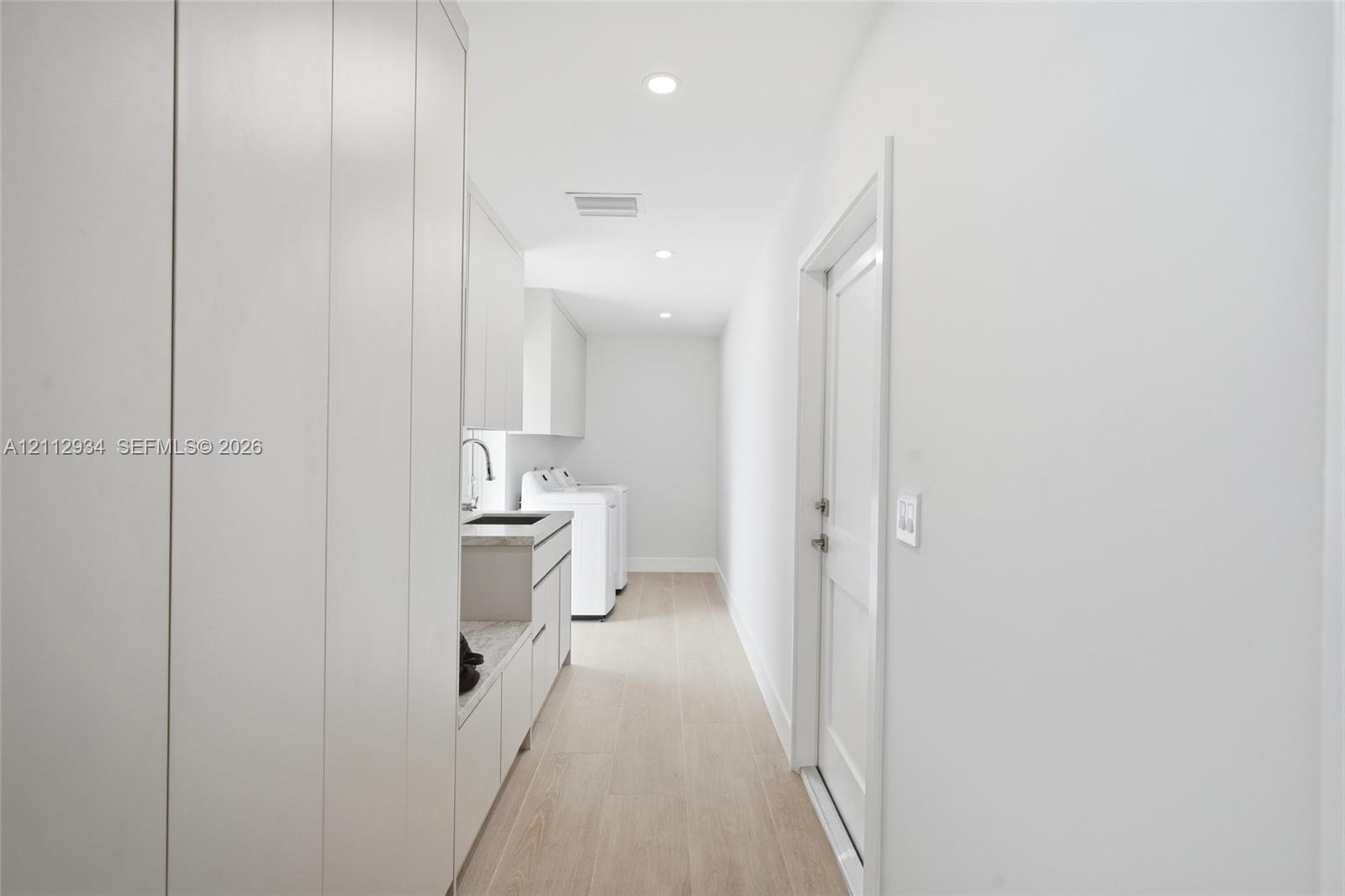 Laundry area featuring full-height white cabinetry, light-toned stone-finish countertops, an undermount sink with a gooseneck faucet, and wood-finish flooring